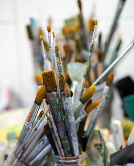 Close-up of a glass jar filled with various paintbrushes, showing their colourful and well-used bristles. Close-up of a glass jar filled with various paintbrushes, showing their colourful and well-used bristles.